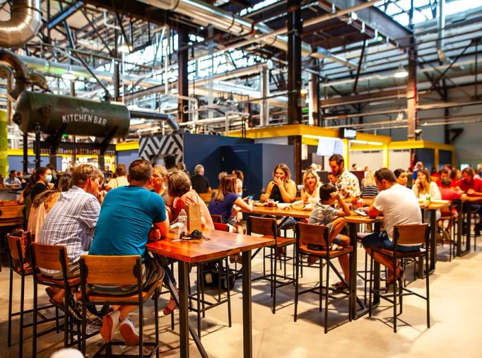 Patrons dine at tables in a spacious industrial setting surrounded by food vendor stalls.