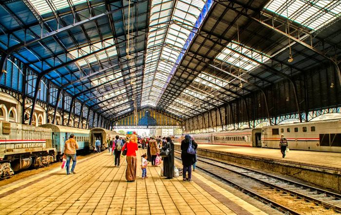 A group of travelers strolls along a train platform beneath a striking glass and steel roof.