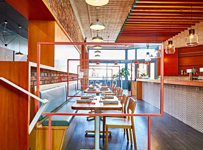 The dining area features teal banquettes and chairs, stylish pendant lights, a bar along one wall, an array of textured materials, and large windows that flood the space with natural light.