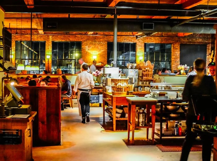 The dining area features an open kitchen with a brick wall and abundant wooden accents, creating a warm and inviting atmosphere.