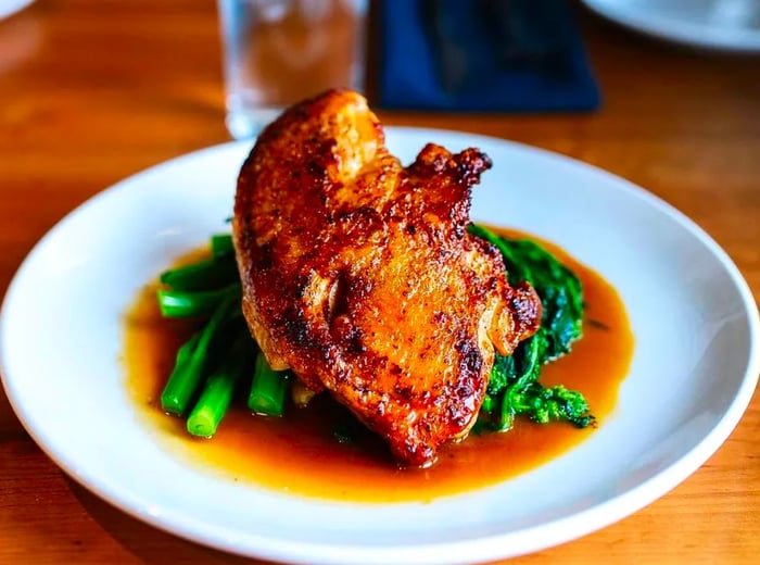 A sizable piece of roast chicken resting on a bed of rapini, surrounded by a rich jus.