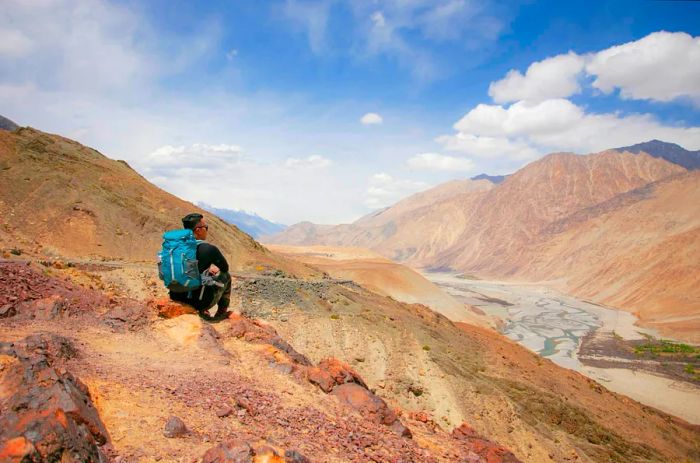 A man rests on the edge of a red rock mountain in the Indian Himalayas.