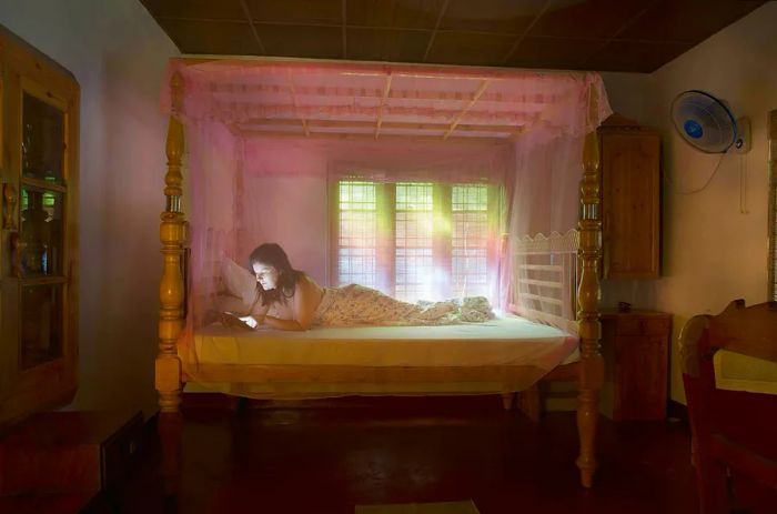 A woman enjoys her time resting on a bed draped with a mosquito net.