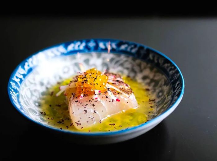 A sizable portion of fish ceviche presented in broth within a small decorative bowl, set against a neutral backdrop.