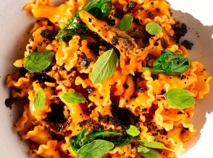 Aerial view of crinkle-edged pasta adorned with basil leaves and dark crumbles.