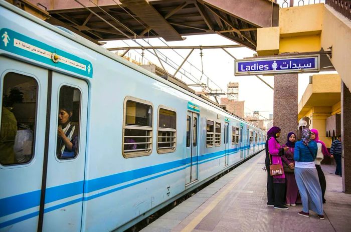 Four women are waiting on a train platform, with female-only symbols displayed above the doors of the approaching train.