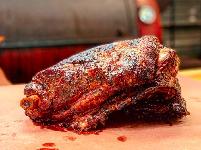 A beautifully presented barbecued lamb shoulder laid out on butcher paper in front of a closed grill.