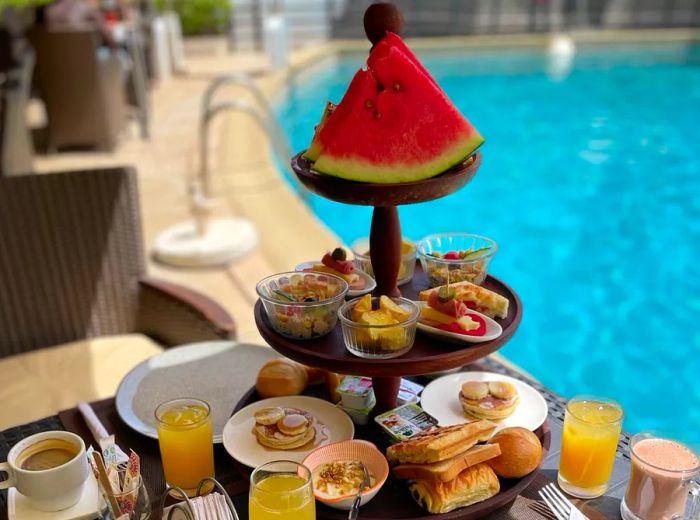 A beautifully arranged tower of brunch dishes topped with a slice of watermelon, set against the backdrop of a pool.