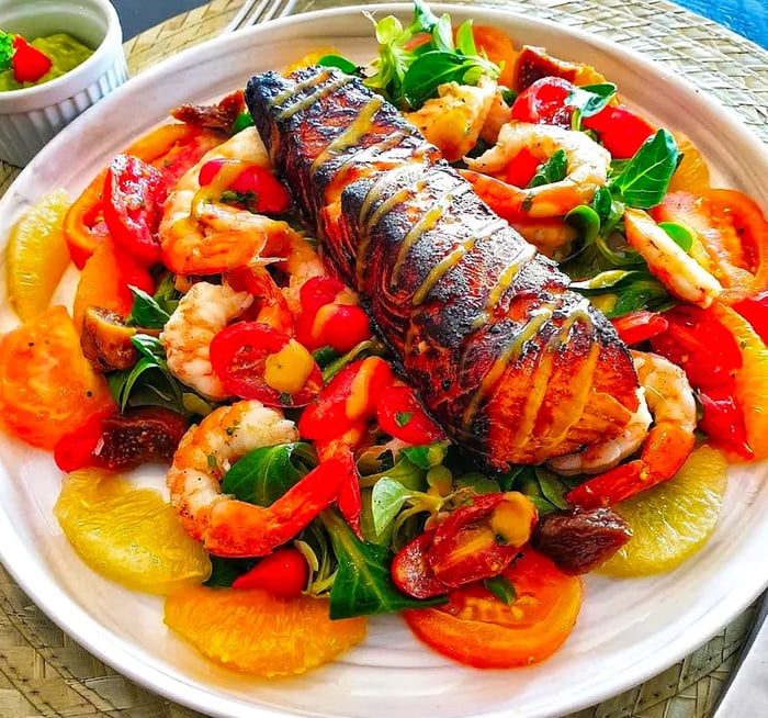 Skewers of perfectly grilled fish served atop a bed of chopped vegetables and shrimp.