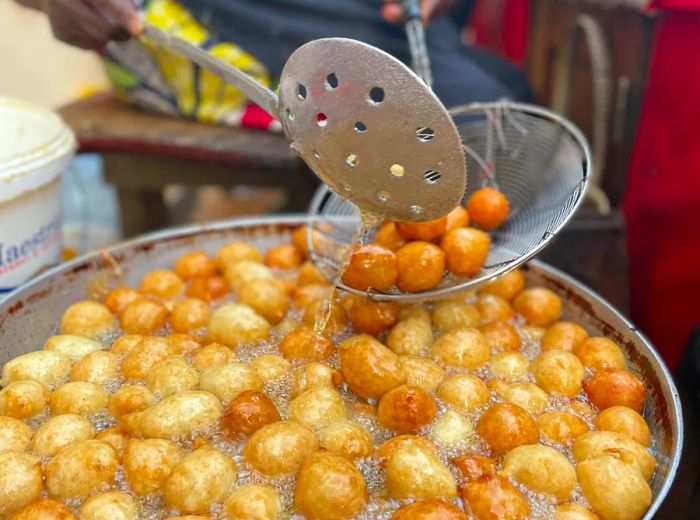 A street chef scoops beignets from a bubbling pot into a strainer.