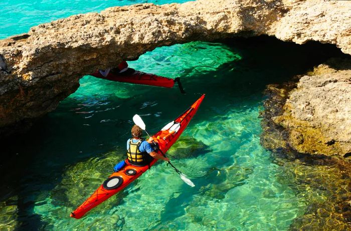 A kayaker gliding beneath a natural limestone arch in the Blue Lagoon, Comino.