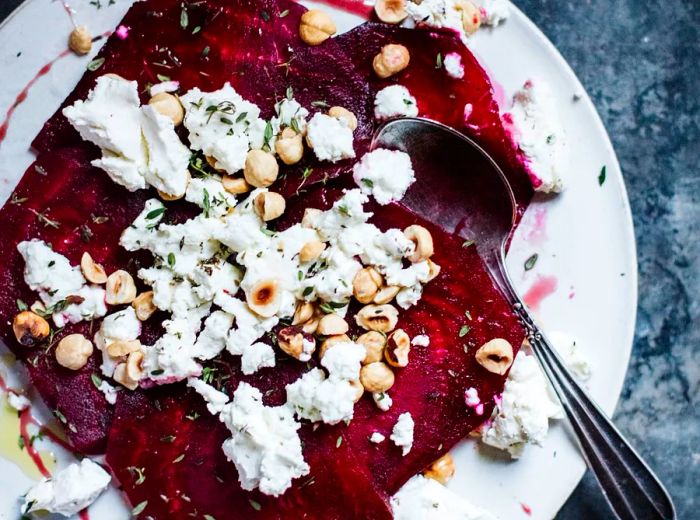 From above, thinly sliced beets adorned with crumbled cheese and fresh herbs.