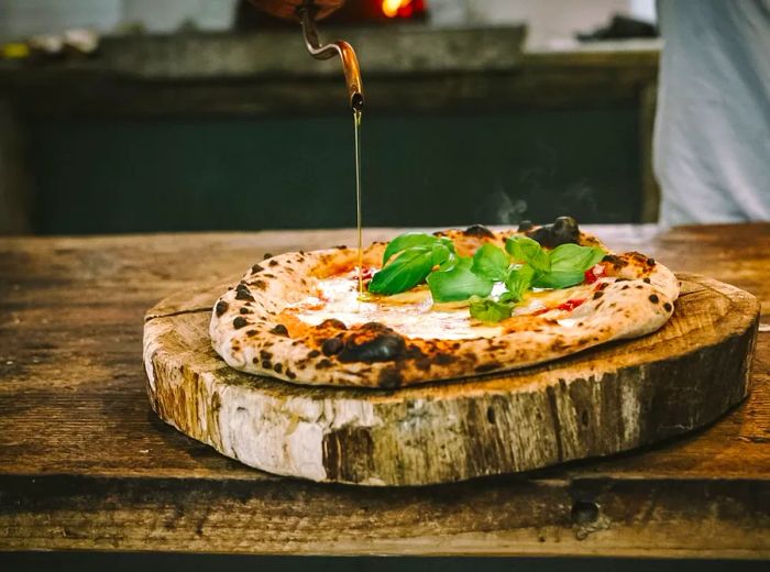 A chef drizzles oil from a metal decanter onto a freshly made pizza.