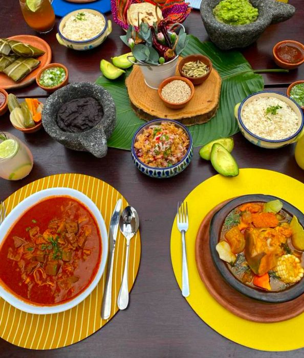 An overhead view reveals an array of stews simmering in pots, accompanied by side dishes, avocados, and various toppings.