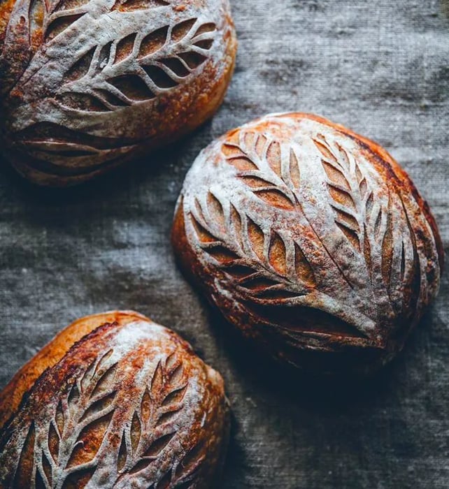 An overhead view showcases several beautifully patterned loaves dusted with flour.