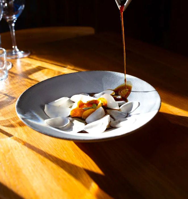 A chef discreetly drizzles sauce over a dish adorned with delicate white petals.