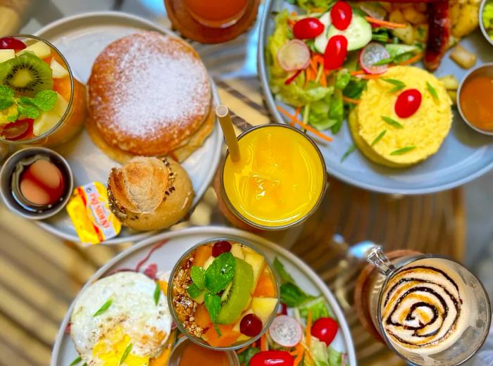 An aerial view of platters featuring eggs with potatoes, fruit salad, pancakes, and sausages.