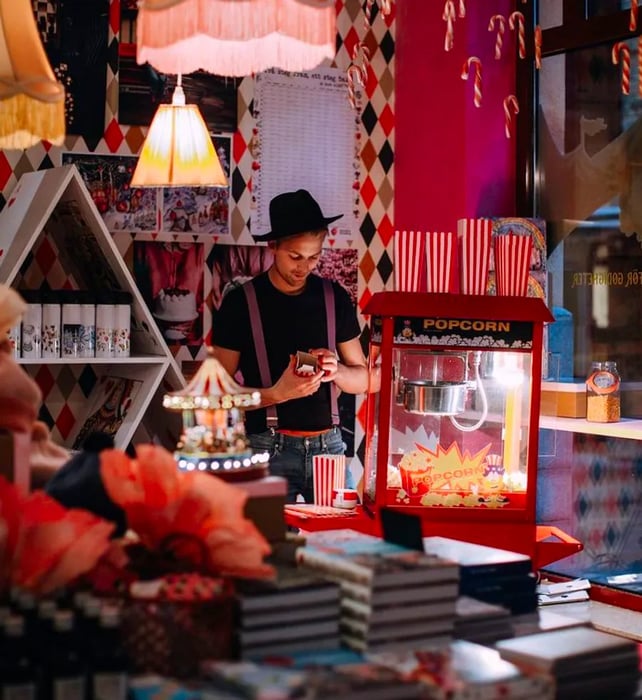 A staff member dressed in carnival attire stands next to a popcorn maker, surrounded by an abundance of quirky decorations.