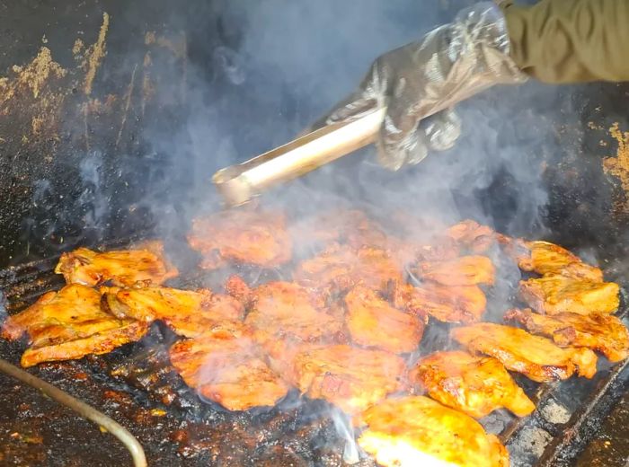 A hand holding tongs hovers over sizzling pork chops on the grill, creating a cloud of smoke.