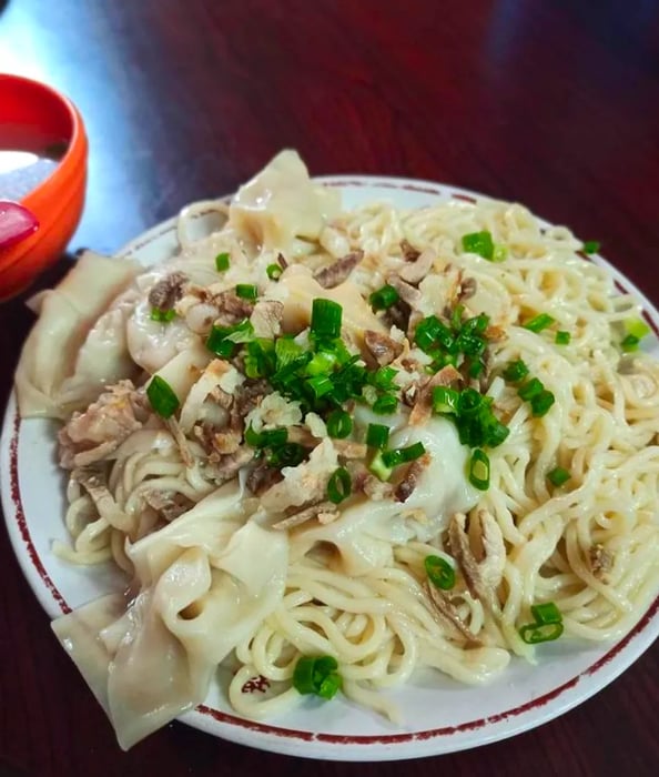 A bowl of noodles adorned with wontons, meat, and greens.