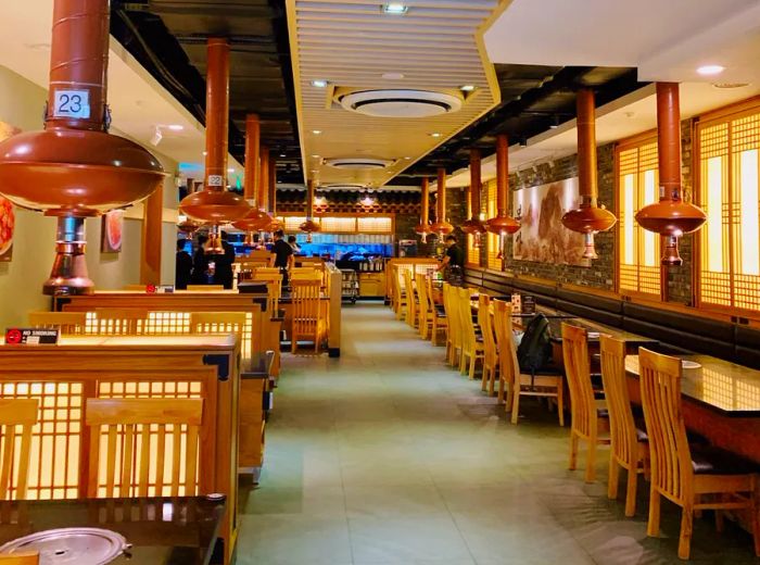 An inviting restaurant interior featuring a long counter and tables equipped with overhead vents for grilling.