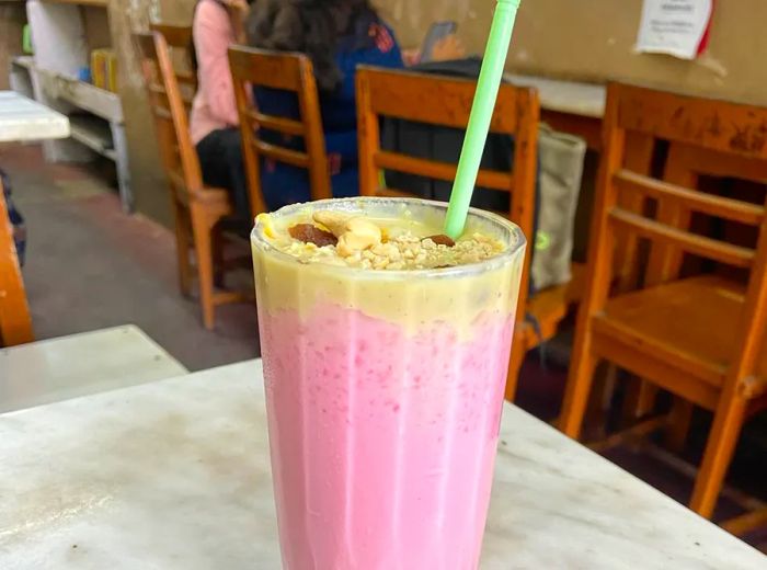 A vibrant pink drink served in a sundae glass, adorned with nuts and a dollop of cream.