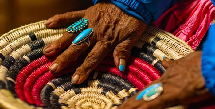 A Navajo woman with turquoise rings gently touches a woven basket