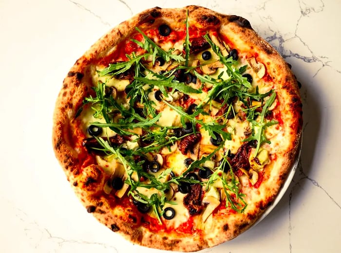 An aerial view of a pizza adorned with greens, olives, and assorted vegetables.