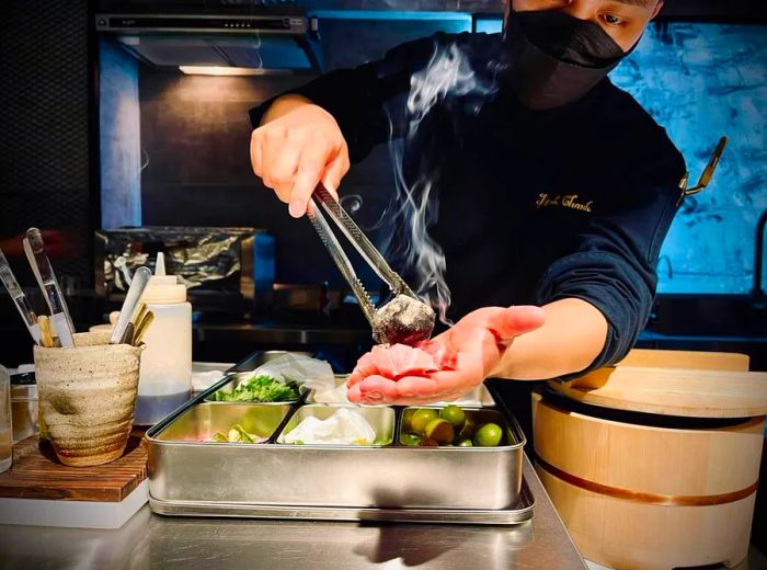 A sushi chef carefully places a hot coal on slices of fish.