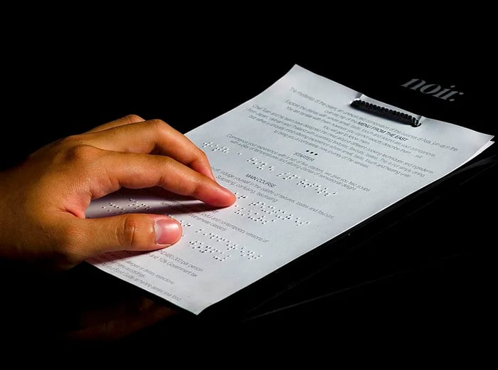 A hand glides over Braille lettering on a menu in a dimly lit room.