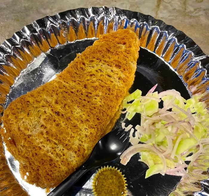 A tin plate featuring a breaded cutlet accompanied by sliced raw vegetables and a small serving of sauce.