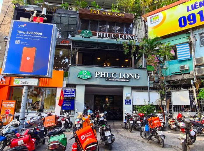 A cafe exterior nestled among a variety of other shops and surrounded by scooters.