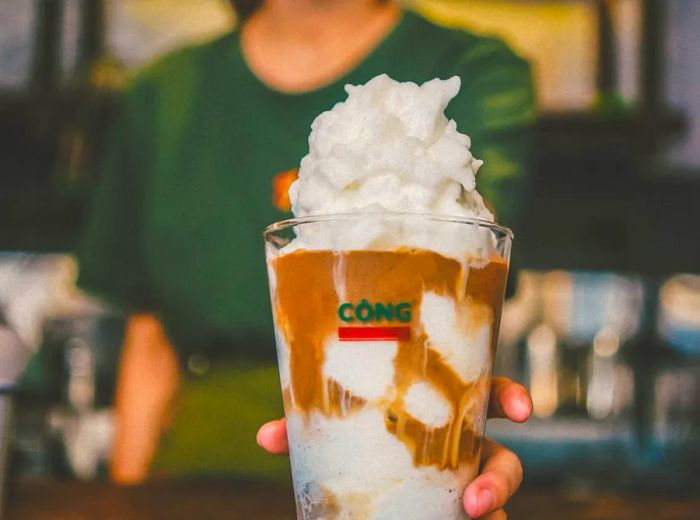 A barista serves a large iced beverage crowned with whipped cream.