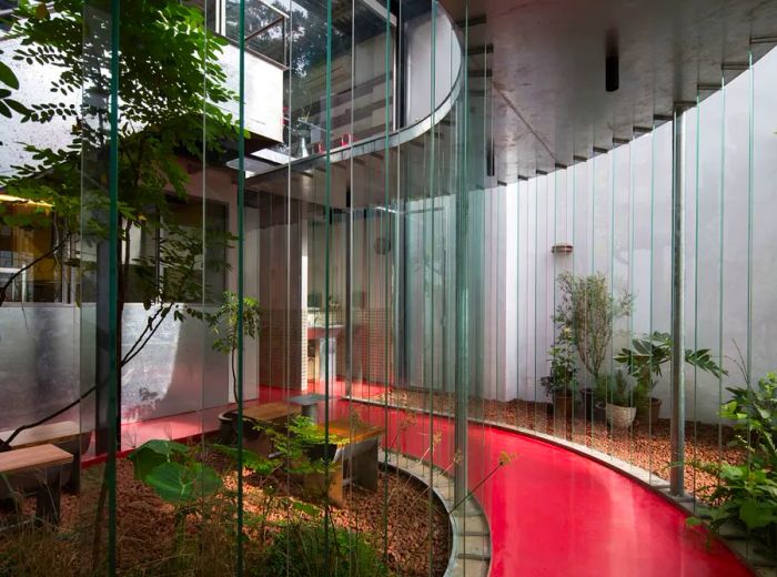 A red pathway winds between slatted glass walls, leading into a modern cement structure.