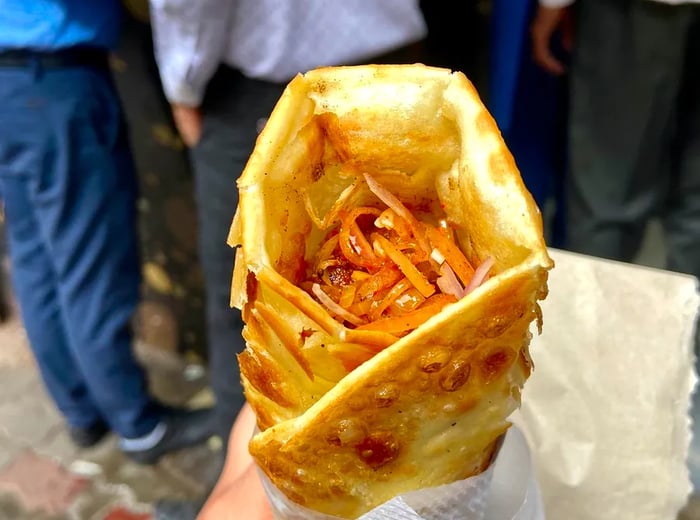 A hand grips a kathi roll wrapped in paper.