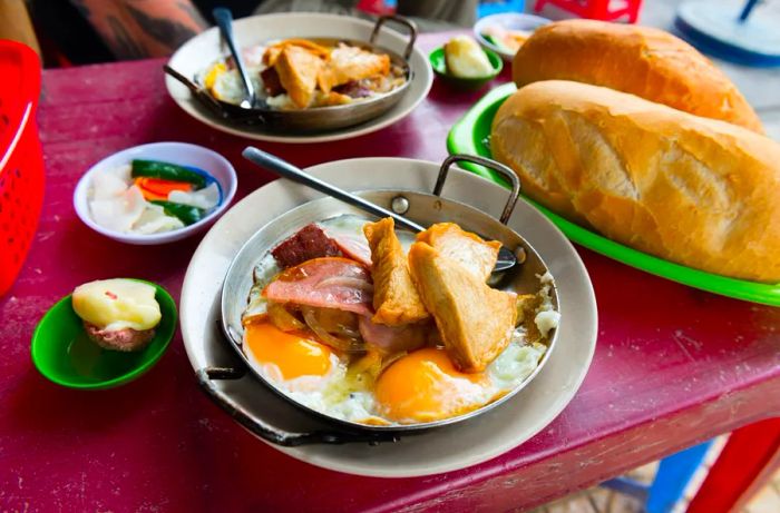 A platter featuring eggs adorned with slices of meat and fried tofu, accompanied by substantial loaves of bread.