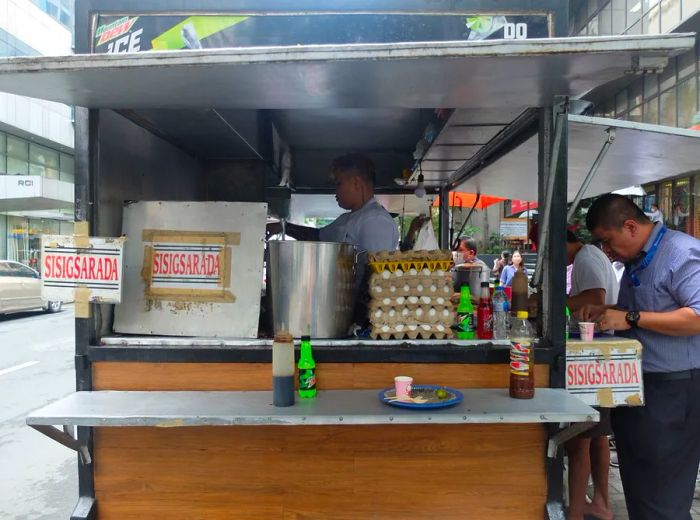 Customers gather at the counter of a metal food cart while a cook prepares meals inside.