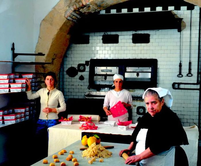 Three bakers are busy at work in a spacious, tiled kitchen.