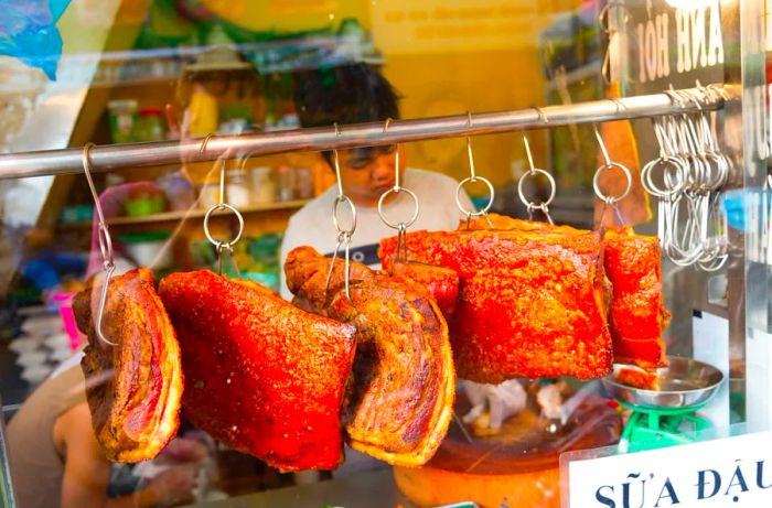 Large chunks of roasted pork dangle on skewers, while an employee works in the background.