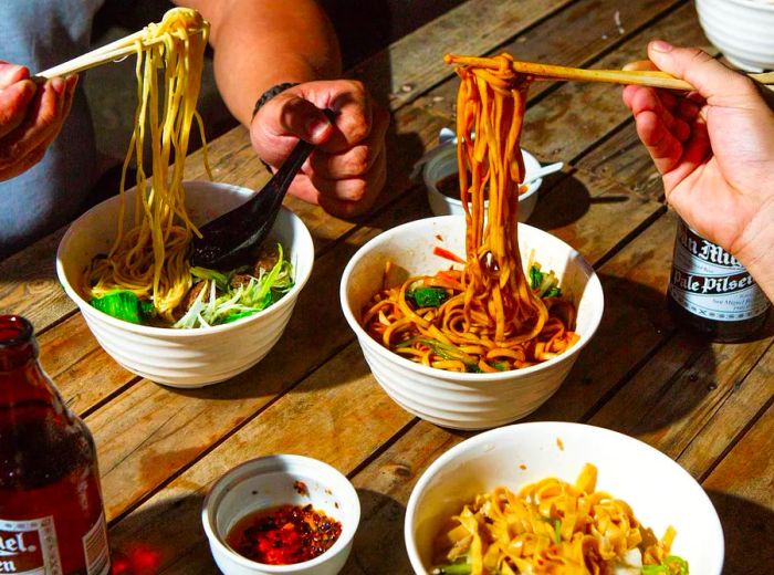 Two patrons lift their chopsticks to enjoy bites of noodles.