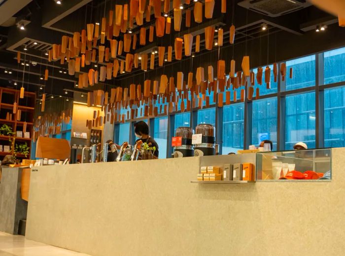 A barista operates behind a coffee counter, under an intricate mobile sculpture.