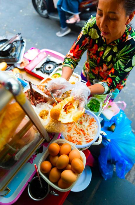 Aerial view of a vendor filling a sliced banh mi baguette with ingredients.