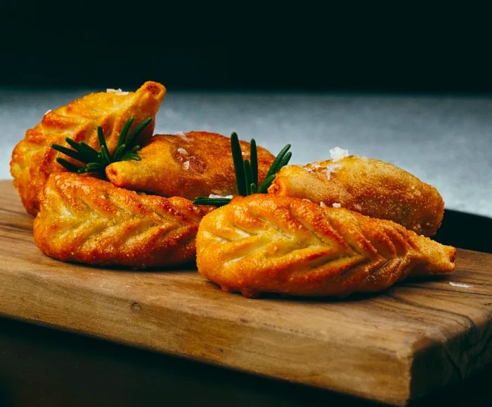 A thick wooden board displays a selection of fried culurgiones, shaped like wheat.