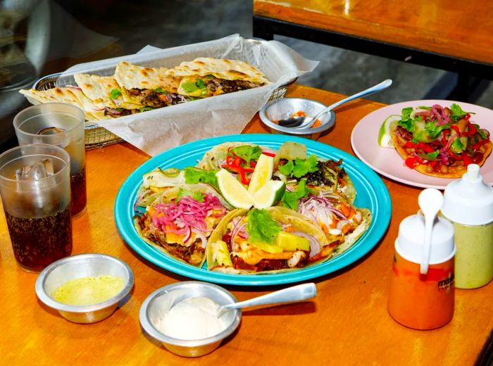 A platter showcasing an assortment of tacos, paired with quesadillas and a variety of beverages.