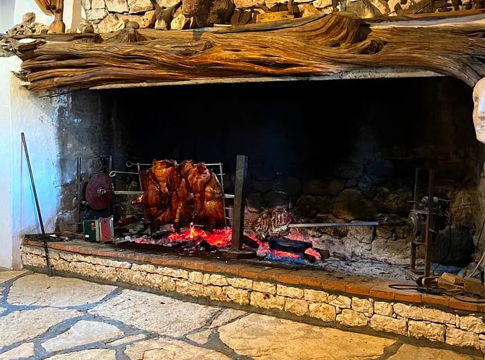 A large stone hearth filled with glowing coals, with roasted meats resting on a rack above.