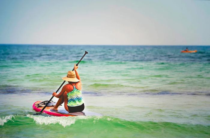 A senior woman paddles on a paddleboard in the shallow waters off the coast of Pensacola, Florida.