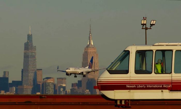 A United Airlines plane approaches the Empire State Building and One Vanderbilt in New York City as it descends, while an AirTrain passes by, Newark Liberty Airport, Newark, New Jersey, USA