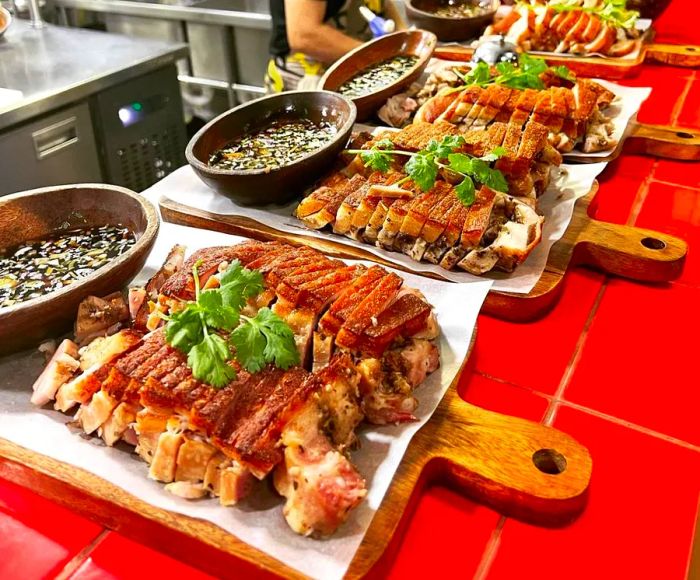 Orders of lechon are neatly arranged on a counter, with a chef busy in the kitchen behind them.