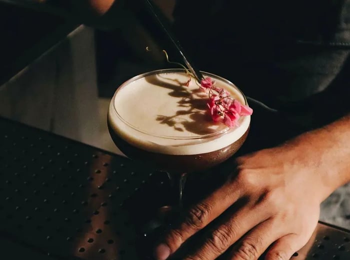 A bartender adds a floral garnish to a cocktail.