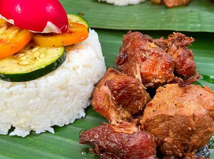 A small serving of chicken adobo accompanied by a mound of rice and vegetables, all presented on a banana leaf.